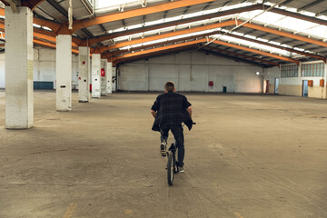 Male riding BMX bicycle inside warehouse navigating between support columns and utility boxes