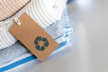 Knitted warm clothes neatly folded heap with craft tag recycling material circle arrow closeup