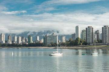 Fototapeta premium Serene Vancouver skyline with sailboats gliding on calm harbor waters, misty North Shore Mountains in the background under partly cloudy skies
