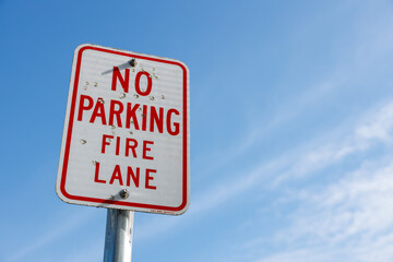Red 'No Parking Fire Lane' sign on weathered metal pole against clear blue sky, highlighting urban traffic rules and emergency access