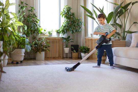 A child helps his parents at home and vacuums the carpet with a hand-held vacuum cleaner.