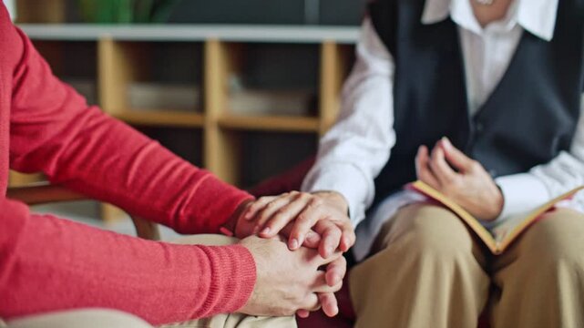 Close-up view of supportive female psychologist holding hands of male patient during emotional moment in therapy session