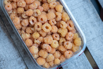 White raspberries in a plastic container on a wooden background, top view. Real photo, selective focus.