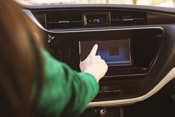 Female driver sitting in car cabin reaching and touching infotainment touchscreen and air vents