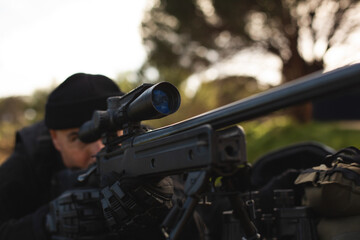 Mature adult male wearing tactical gear lying in park clearing aiming rifle scope mounted on bipod