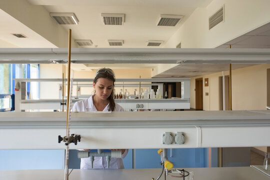 Female scientist standing behind laboratory bench in chemistry lab, inspecting reagent bottles