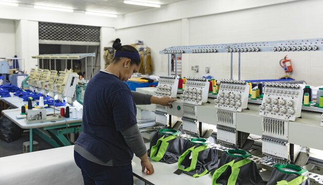 Woman adjusting multi-head embroidery machine controls inside workshop with thread spools and caps