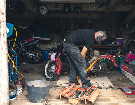 Middle-aged man grinding fender in garage using electric angle grinder sending sparks, copy space