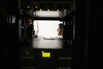 Male technician inspecting network switches inside rack with blinking LEDs and earpiece, copy space
