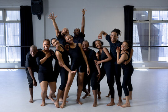 Diverse dance troupe practicing choreography in black attire at dance studio with barre and speaker