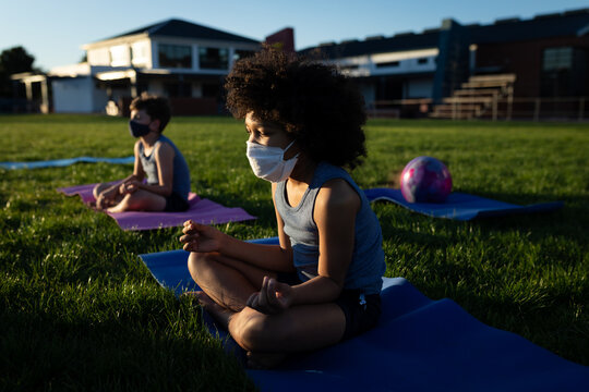 Diverse male students meditating on yoga mats with colorful ball at grassy schoolyard, copy space - Powered by Adobe