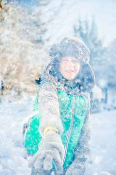 School-age boy extending gloved hand in snowy clearing wearing trapper hat and vest with backpack