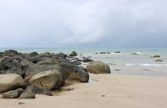 Smooth dark rocks boulders and calm ocean waves under a cloudy sky at Mission Beach in Queensland, Australia - Powered by Adobe