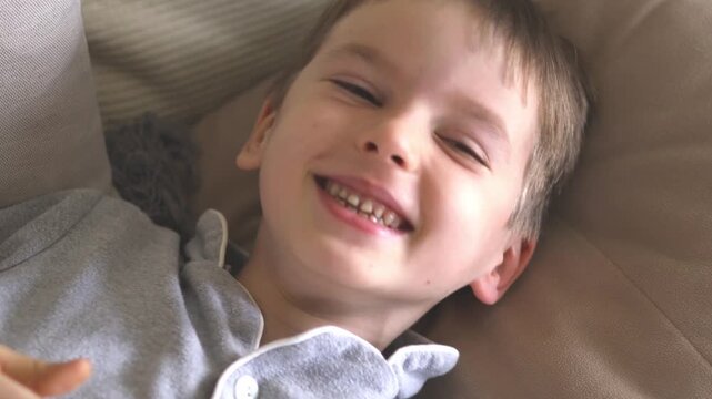 Little boy of six years old in grey pajamas lies in bed and laughs. 