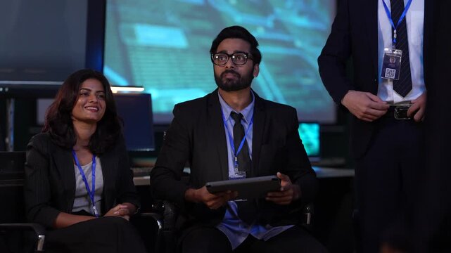 Intelligence analysts in a government command center receive a mission briefing, observing critical data on a large video wall before a surveillance or security operation.