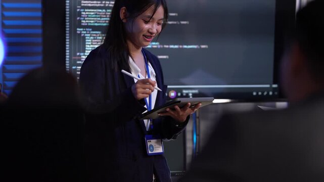 A female tech lead or scrum master leads a sprint planning meeting, explaining the codebase on a large screen and outlining new features for her development team in an agile company.