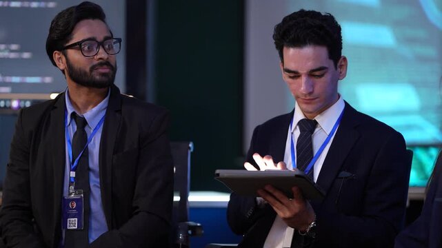 At a future AI developer summit, engineers watch a live model training session on screen while one attendee uses a tablet for real time prompt engineering and interaction with the new LLM.