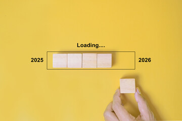 Loading Progress Bar from 2025 to 2026 with Wooden Blocks. A hand places wooden blocks in a row, creating a progress bar transitioning from 2025 to 2026, symbolizing the new year and future progress
