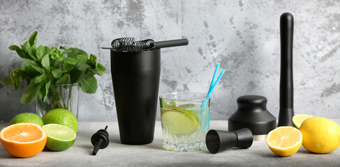 Glass of cocktail with bartender's utensils, citrus fruits and mint on grey grunge background