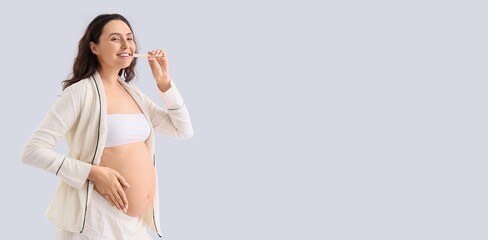 Pregnant woman brushing teeth on light background with space for text