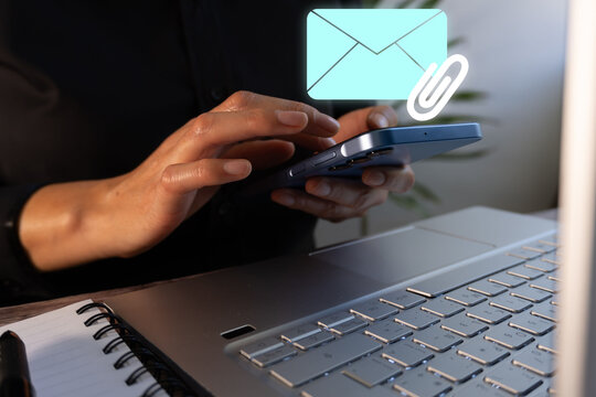 Businesswoman in front of her computer keyboard and a cell phone with an email icon with an attachment