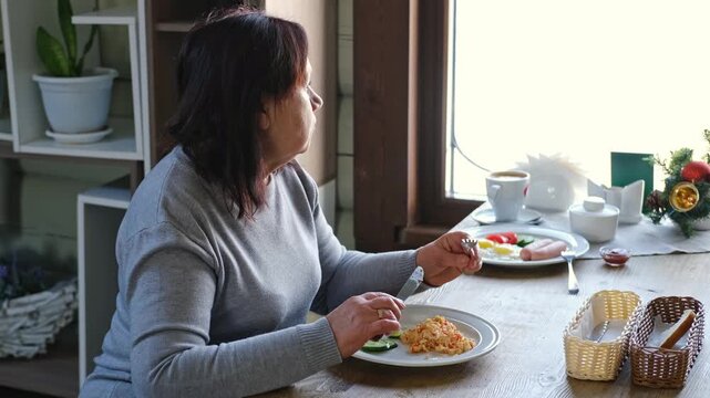 Happy senior woman eating a scramble on a white plate with vegetables. Elderly lady using knife and fork to cutting meal, has a breakfast. Balanced diet, cooking, culinary. Food concept. Old woman