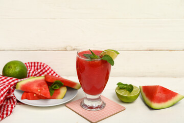 Glass of fresh watermelon juice with lime and mint on white wooden background