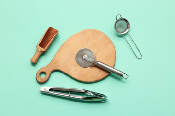 Set of kitchen utensils with stainless steel pizza cutter on color background