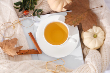 Composition with cup of green tea, notebook, sweater and autumn leaves on light fabric as background