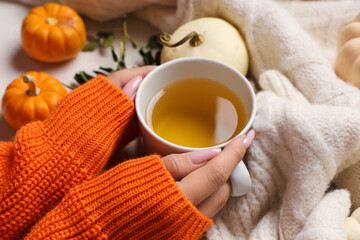 Female hands with cup of green tea, pumpkins and sweater on white background, closeup