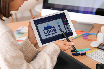 Young female designer working with tablet computer at table in office, closeup