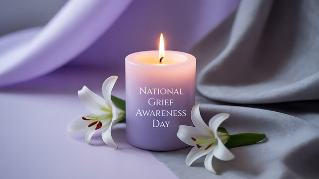 A lit candle with 'National Grief Awareness Day' text, surrounded by white lilies on a soft purple and gray fabric background.
