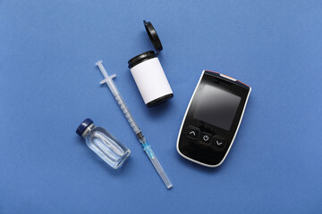 Glucometer with insulin on blue background. Diabetes concept