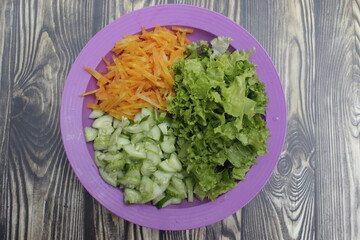 Slices of fresh carrots, cucumbers, and lettuce on a plate on a wooden table. A healthy meal.