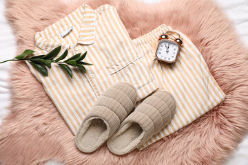 Stylish pajamas with slippers and alarm clock on bed