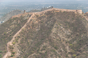 Ancient Fortification Wall Ascending a Steep Scrub-Covered Hillside to a Watchtower in Rajasthan © shijo