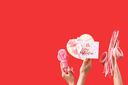Female hands with sex toys, gift and card on red background. Valentine's Day celebration - Powered by Adobe