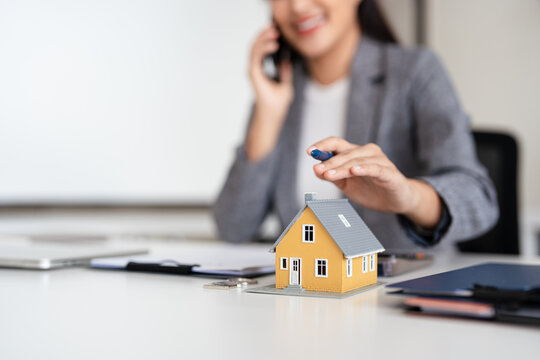 Confident asian business lady, broker real estate agent or manager, sitting at table in a modern office, working with laptop, talking to client or employees on smartphone, smiling.