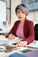 Interior designer working on her project  in studio office holding pen taking notes in a notepad .