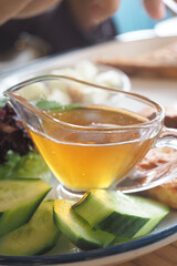 A clear bowl holds honey syrup dressing beside fresh cucumber and salad