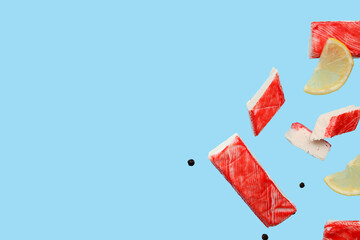 Cut tasty crab sticks with peppercorns and slices of lemon flying on blue background © Pixel-Shot
