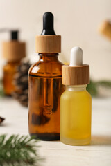 Bottles with coniferous cone essential oil on white wooden background