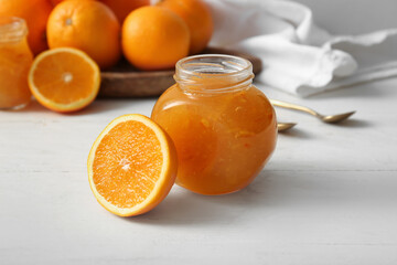 Jar of tasty orange jam on white wooden background