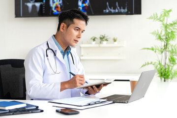 Serious mature professional  doctor using laptop computer in hospital office watching medical webinar training, writing in healthcare report, consulting patient online at telemedicine meeting.