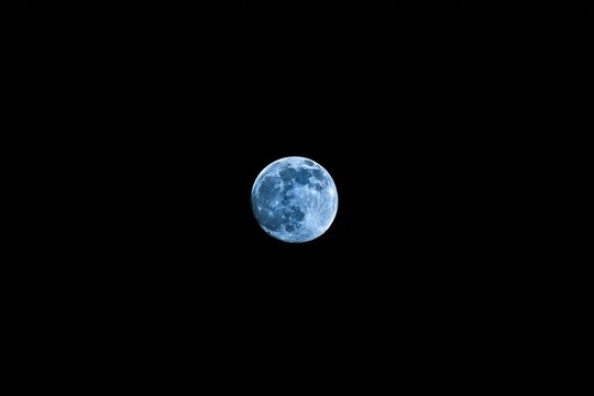 Full bluish moon against a black sky - Powered by Adobe