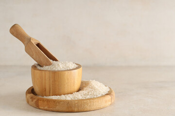 Wooden tray and bowl of raw rice with scoop on light background