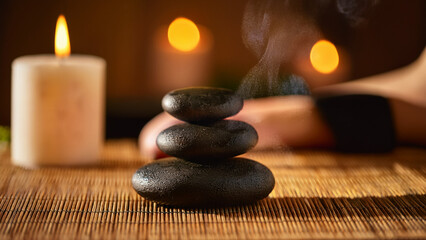 Smooth black basalt stones placed on the back of a client, soft steam rising, warm ambient light with golden and brown tones, bamboo mats and candles in background, close-up perspective focusing on te