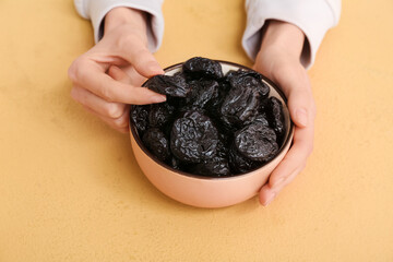 Female hands with bowl of dried prunes on beige background