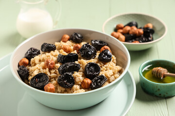 Bowl of tasty oatmeal with prunes, hazelnuts and honey on green wooden background