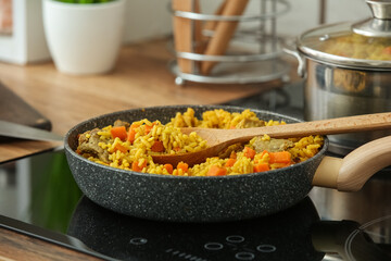 Frying pan with tasty pilaf and spatula on stove in kitchen, closeup